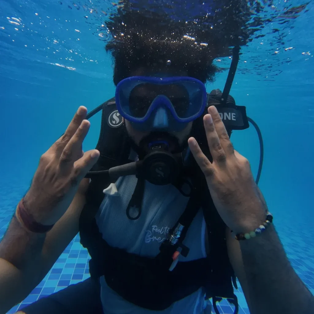 A FlyingFish diver in mask and regulator making a peace sign underwater in Goa