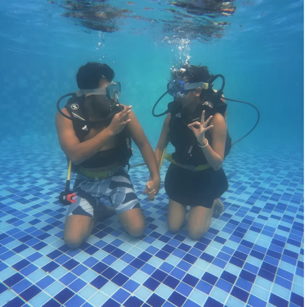Two first-time divers kneeling on the pool floor during scuba training at Novotel, Goa