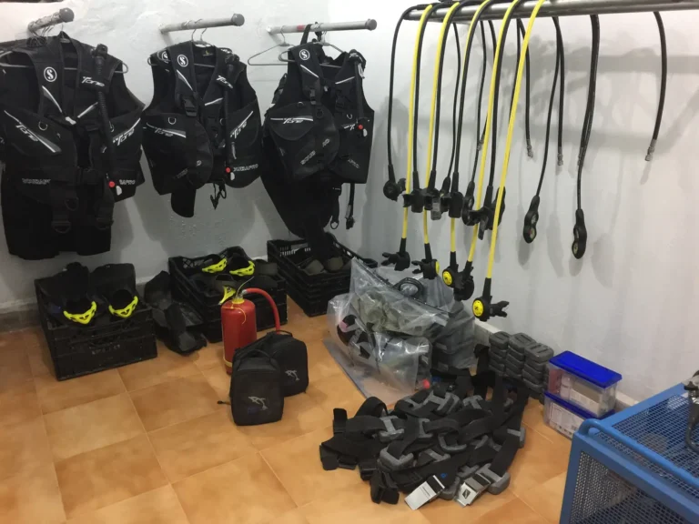 BCDs and regulators hang on racks above crates of fins, weight belts and boots in the gear room