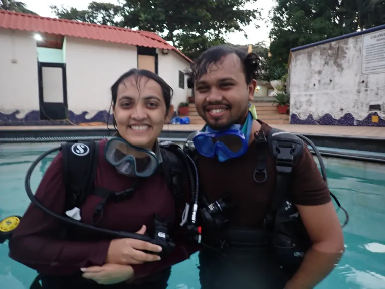 Smiling couple stand in the resort pool in BCDs with masks pushed up after their session