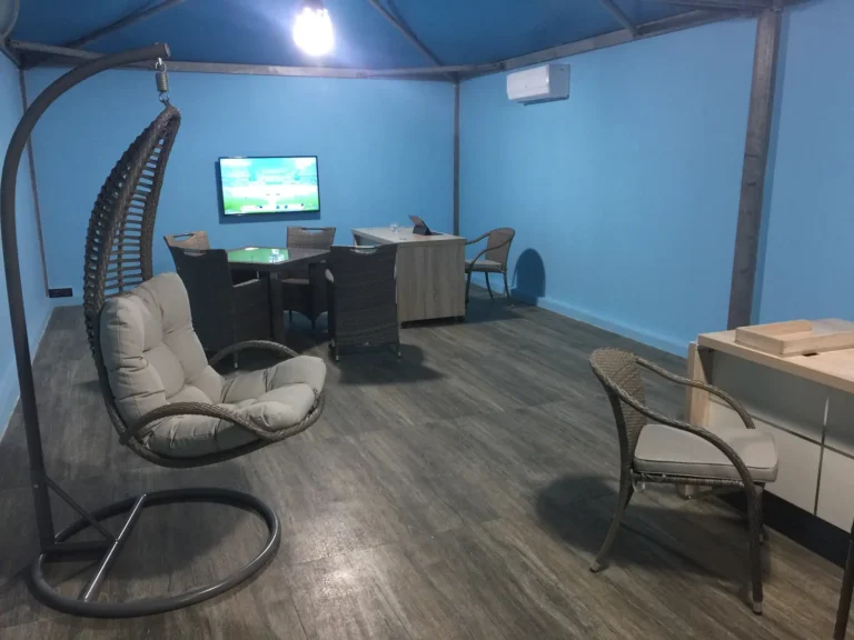 Blue-walled dive centre room with a hanging wicker chair, TV screen and tables for briefings