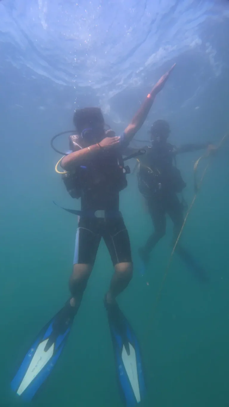 Diver striking a dab pose seen from below in blue water, with a second diver beside a line