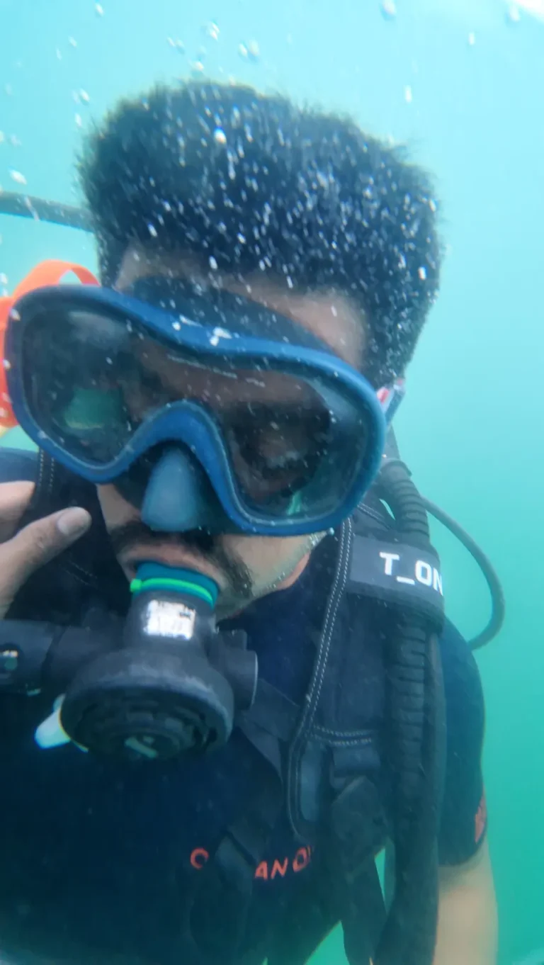 A diver in a dark blue mask takes an underwater selfie as bubbles rise from his hair