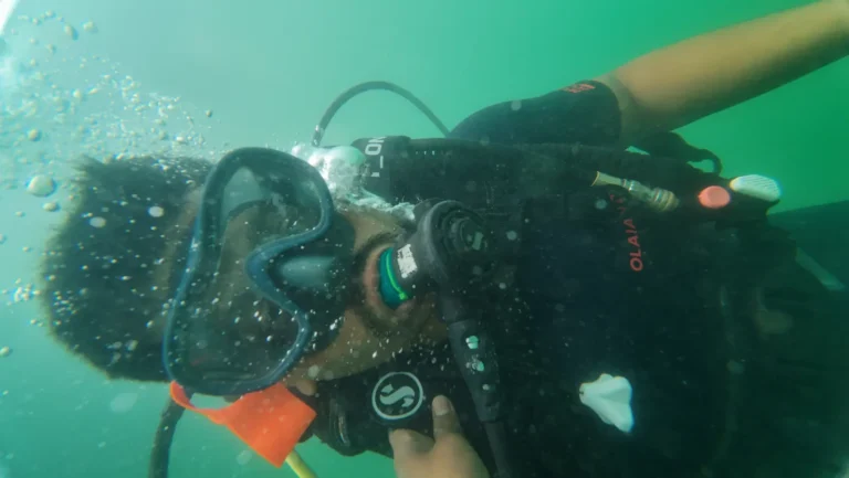 Diver takes a close selfie in green water, mask and regulator framed by bubbles