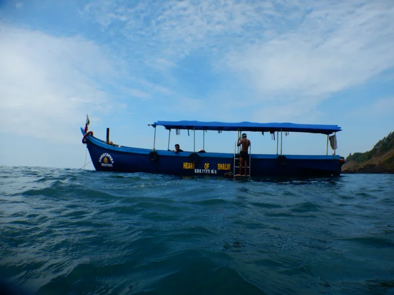 Blue wooden dive boat at anchor seen from water level, a diver climbing the ladder