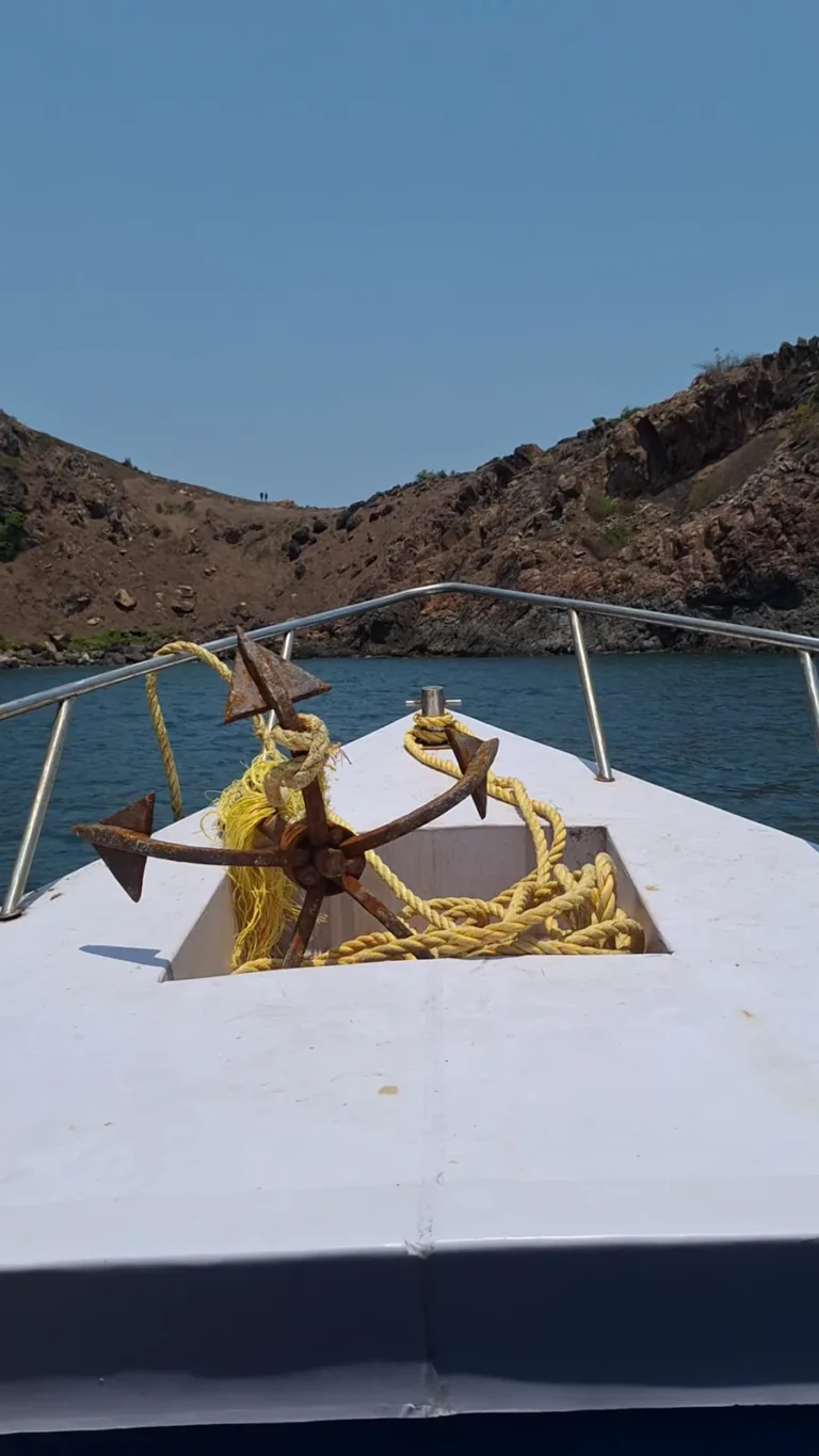 Boat bow with a rusty anchor and rope approaching a rocky cove