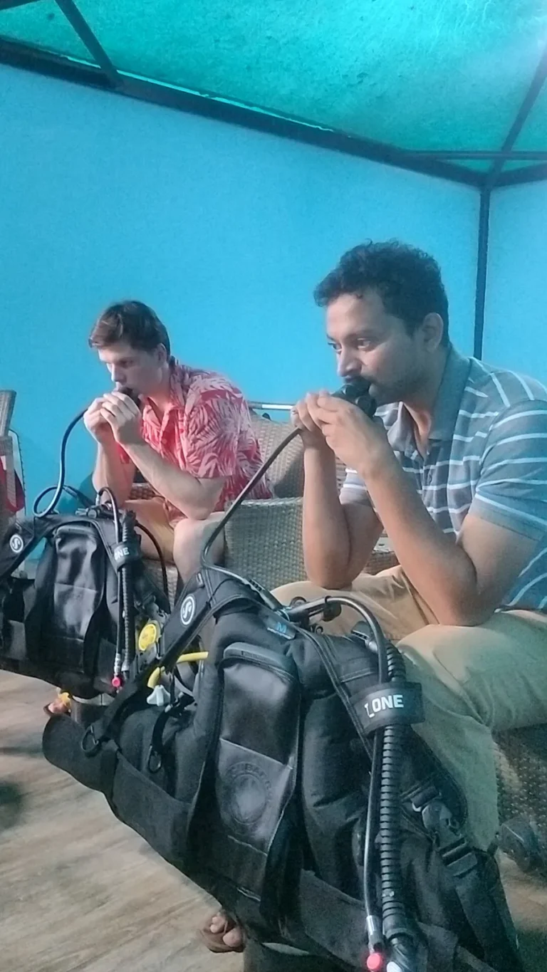 Two guests practising breathing from regulators with BCDs during a dry briefing