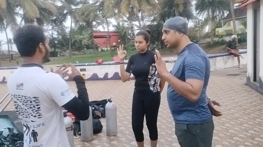 Instructor giving a hand-signal briefing to two guests on the pool deck
