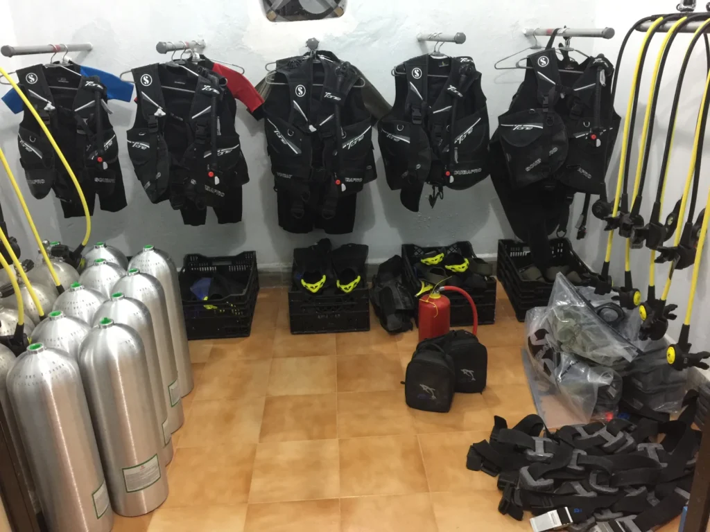 Gear room with Scubapro BCDs on hangers, aluminium cylinders, regulators and fins in crates