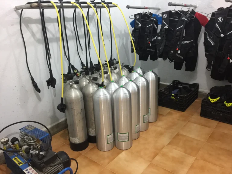 Rows of aluminium cylinders, hanging regulators, Scubapro BCDs and a compressor in the gear room