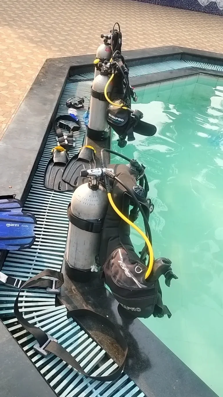 Two assembled scuba sets with fins and masks laid out on a pool edge