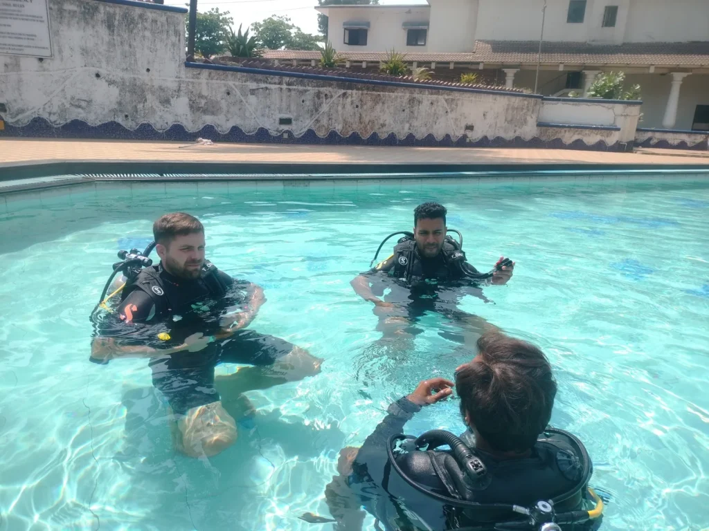 Instructor seen from behind briefing two male students in scuba gear in the Novotel pool