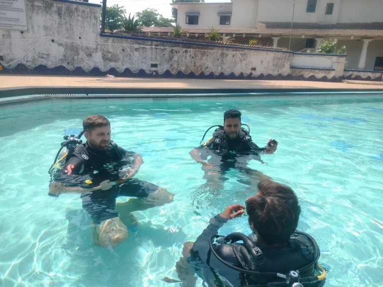 Instructor seen from behind briefing two male students in scuba gear in the Novotel pool