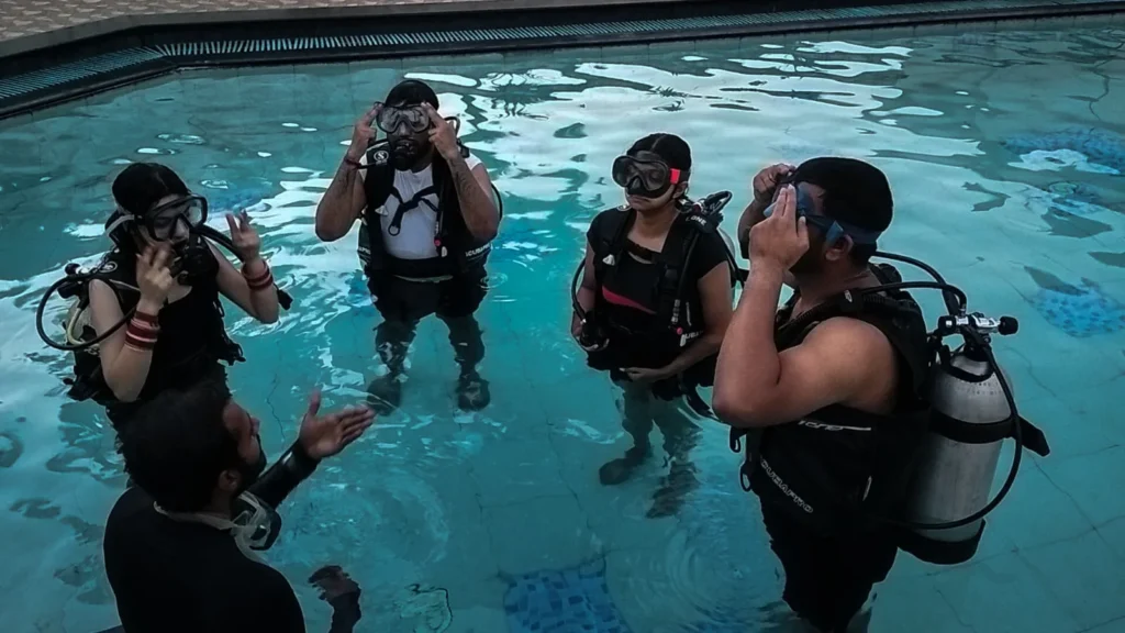Four students in scuba gear in a resort pool while an instructor briefs them