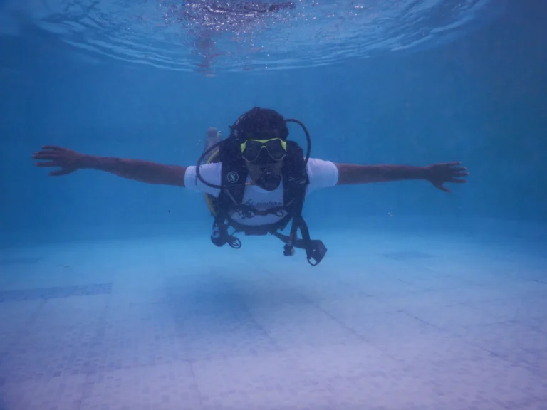 Diver hovering in a pool with arms outstretched, wearing a white FlyingFish T-shirt