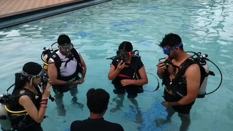 Instructor briefs four students in scuba kit standing in a pool