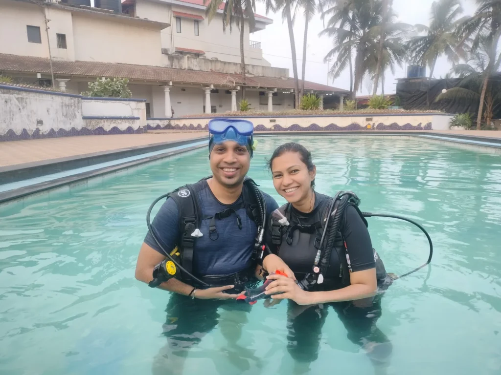 Smiling couple in scuba gear standing in a resort pool