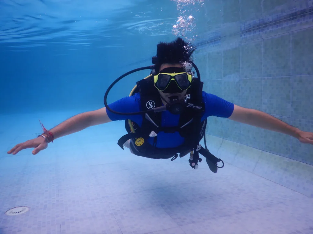 Diver in a blue rash vest gliding horizontally in a clear pool with arms spread