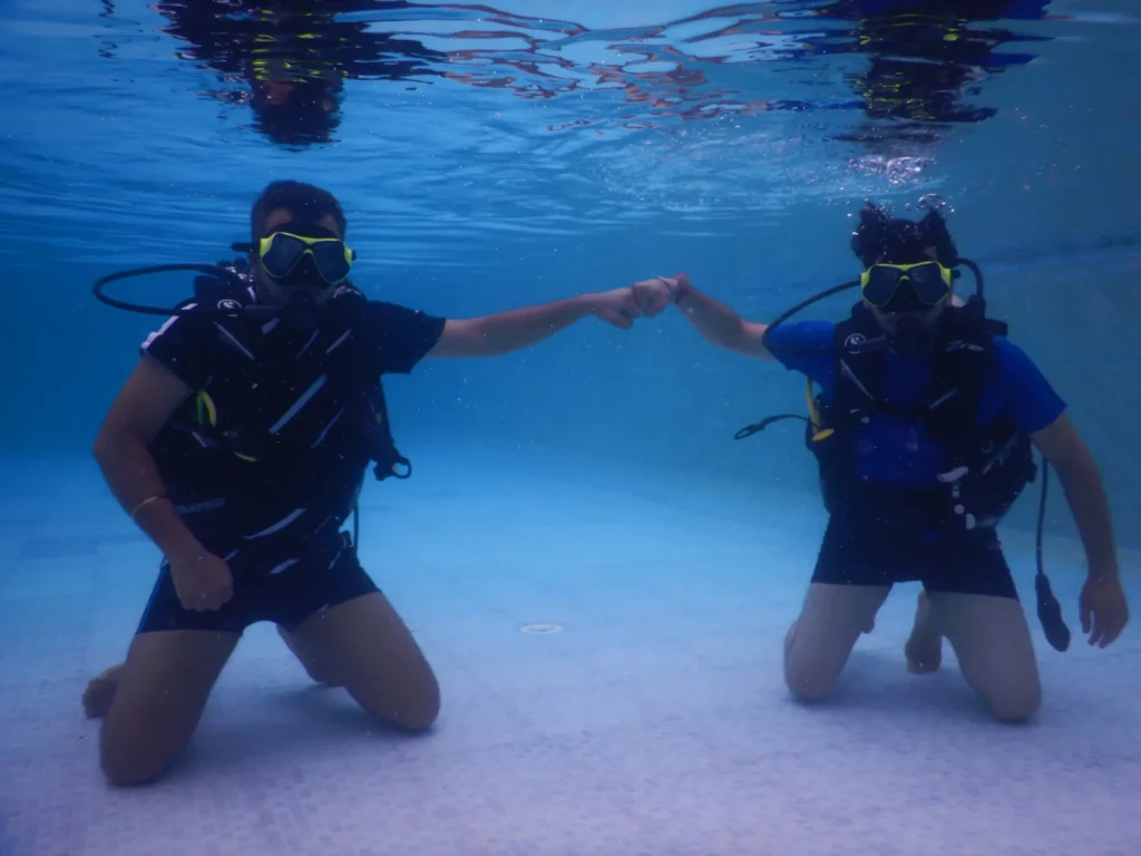 Two divers kneeling on the pool floor bumping fists