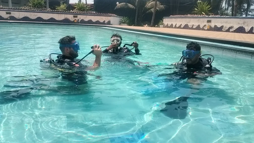 Three divers in scuba gear practising in a bright blue hotel pool