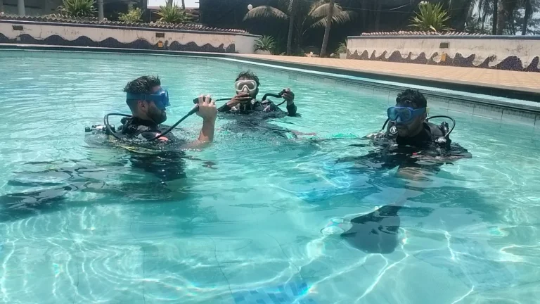 Three divers in scuba gear practising in a bright blue hotel pool