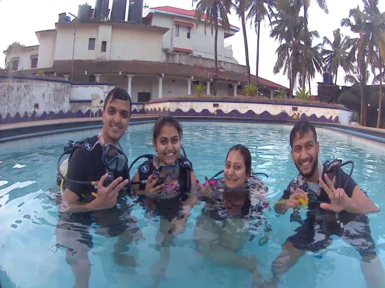 Four smiling students in BCDs standing in a training pool with palms behind