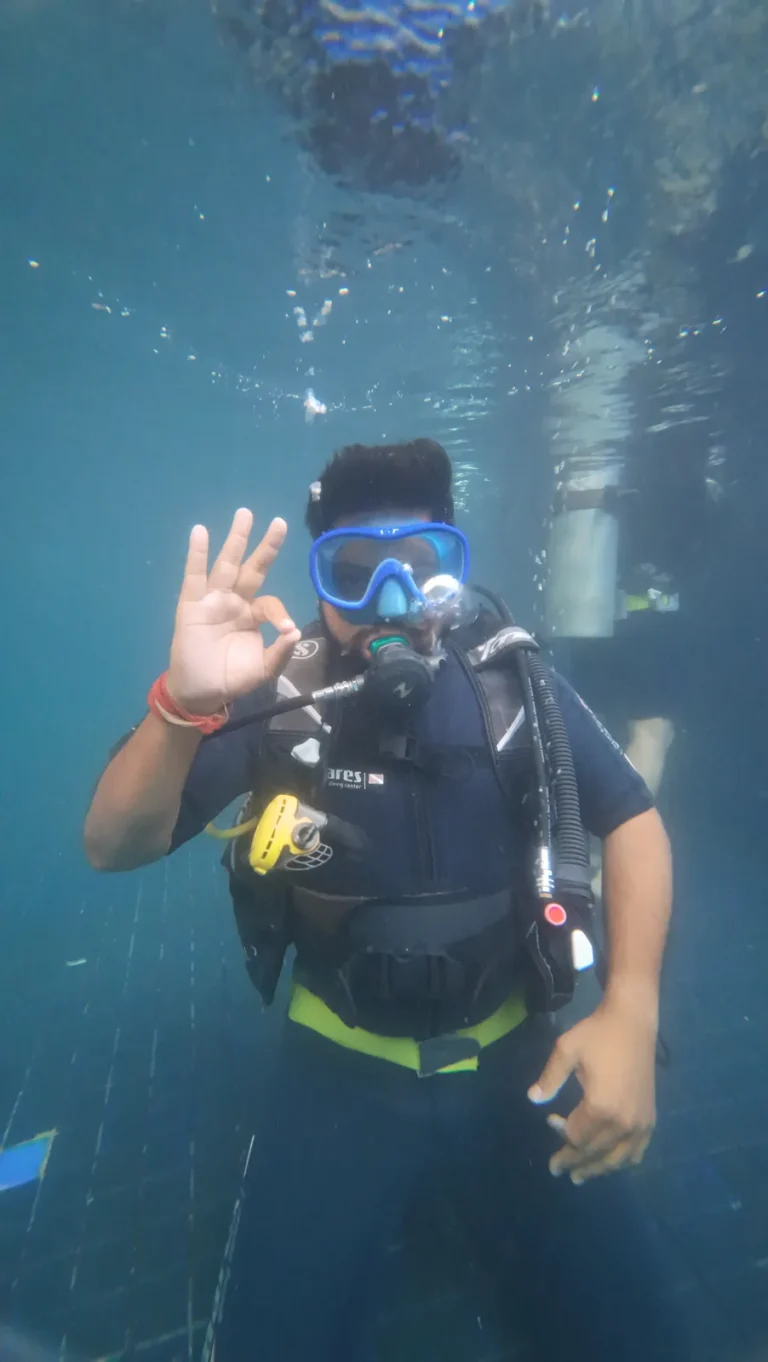 Diver hovering in a deep tiled pool giving an OK sign