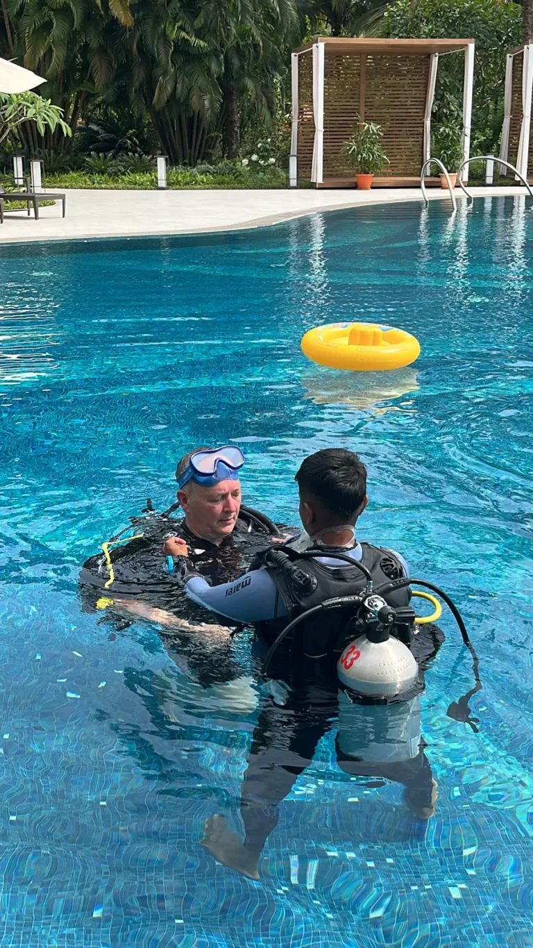 Instructor guiding an adult student in scuba gear in a bright blue resort pool