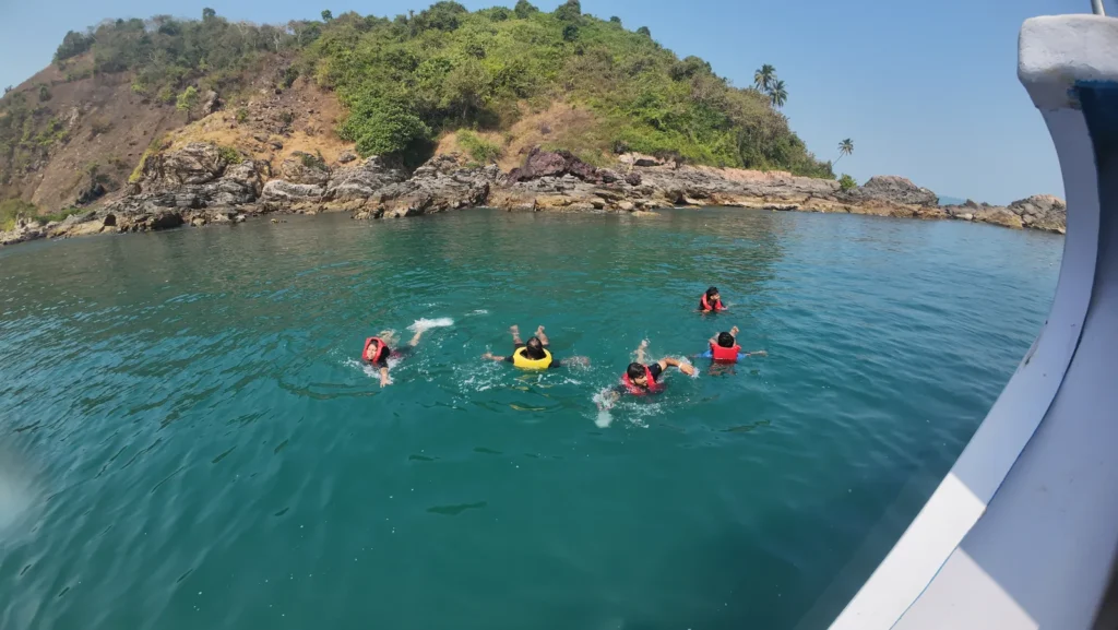 Snorkelers in life jackets swimming in turquoise water near a rocky green island, seen from a boat