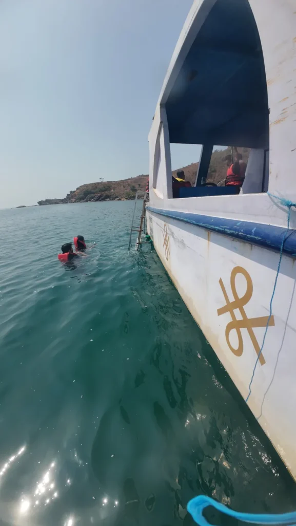 Snorkeler in the water beside a white boat, with an island in the distance