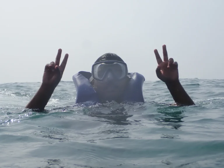 Snorkeler in a life jacket making peace signs at the sea surface