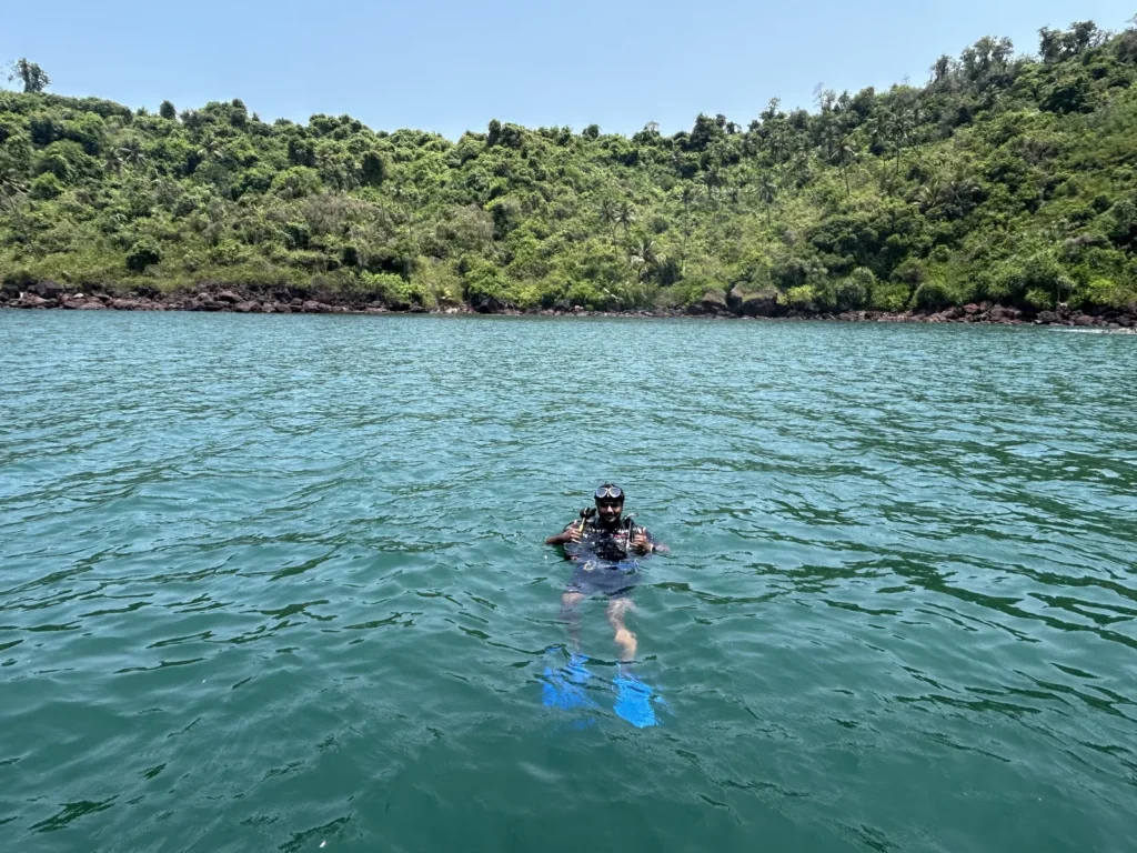 Diver floating at the surface in green water in front of a jungle-covered island