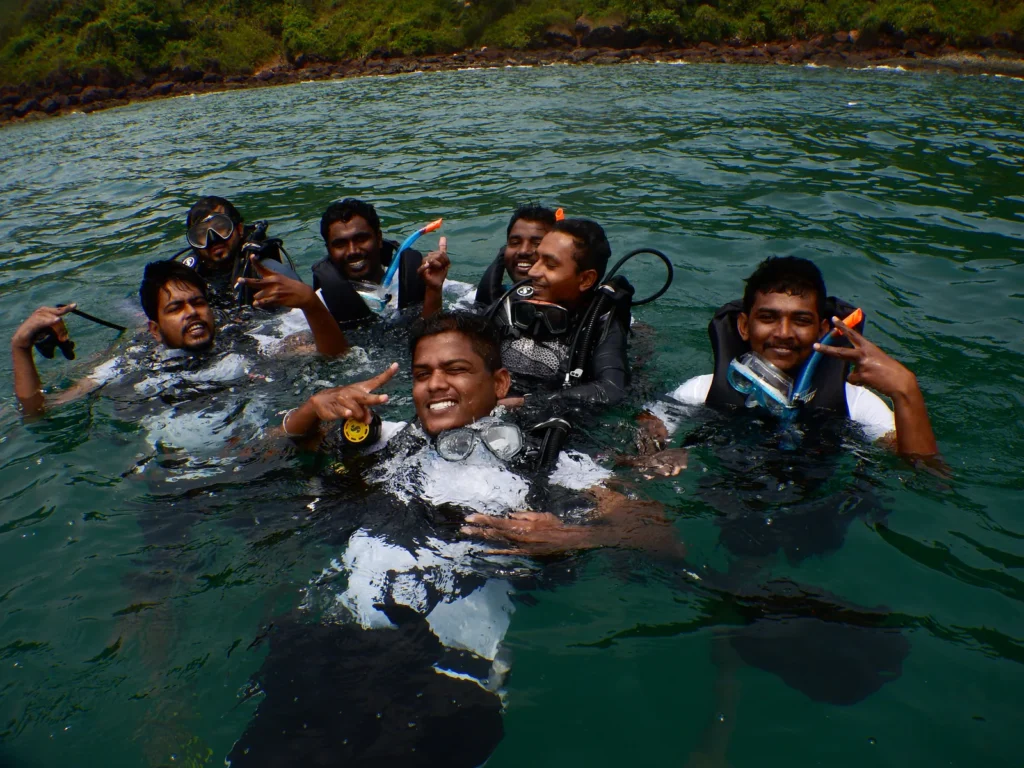 Group of smiling divers in scuba gear at the sea surface near a green island