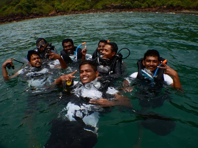 Group of smiling divers in scuba gear at the sea surface near a green island