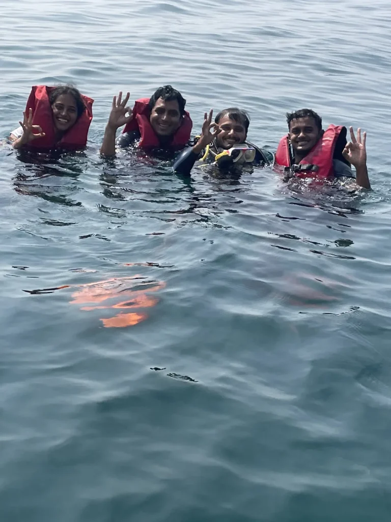 Four smiling guests in life jackets giving OK signs in the sea