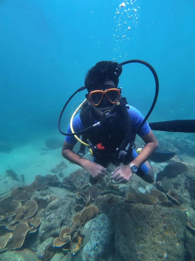 Diver in an orange mask posing over plate corals in clear blue water