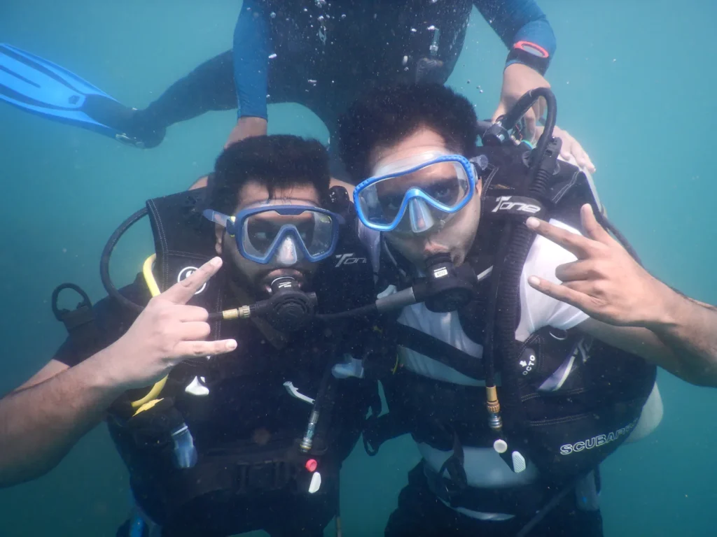 Two divers posing with rock-on signs underwater while a third diver hovers behind