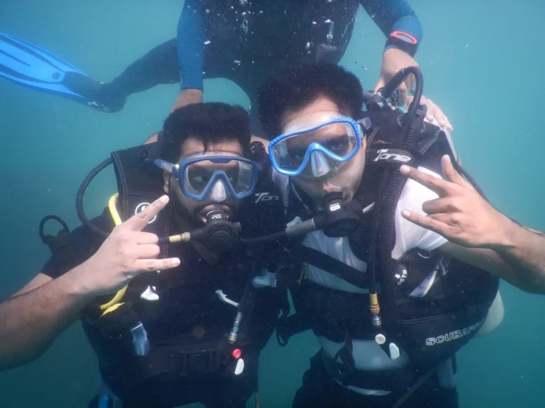 Two divers posing with rock-on signs underwater while a third diver hovers behind