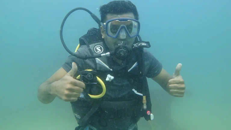 Diver in a Scubapro BCD gives two thumbs up underwater in turquoise water