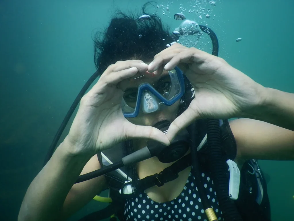 Female diver making a heart shape with her hands underwater around her mask