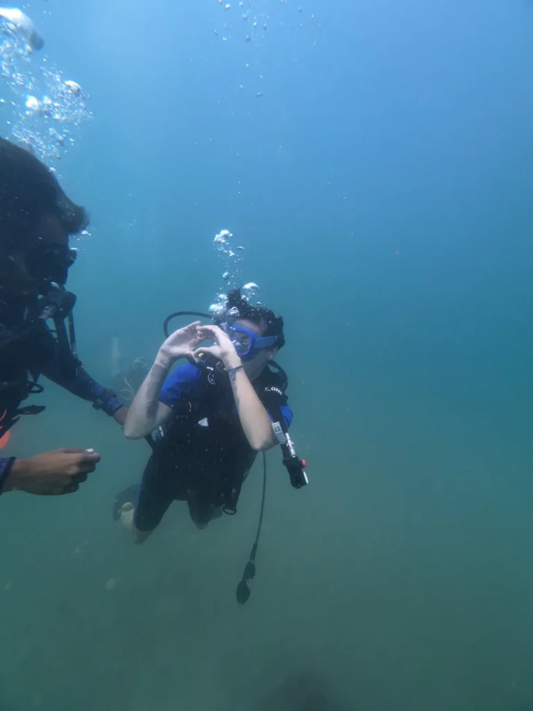 Diver making a heart sign with her hands while an instructor hovers alongside underwater