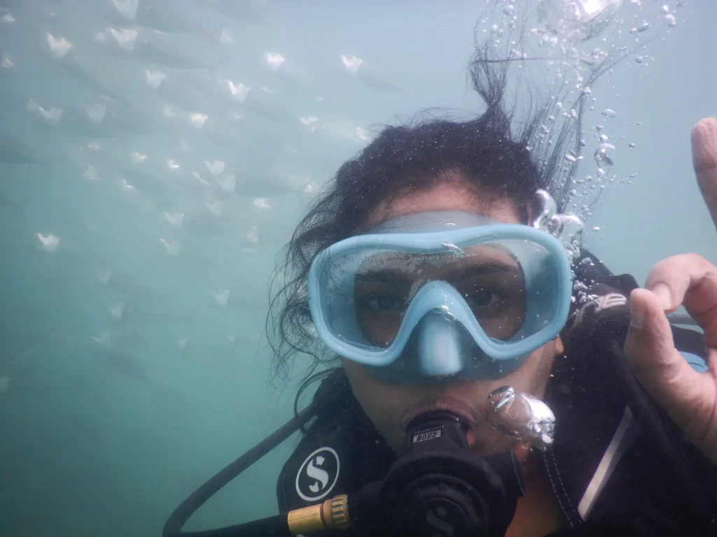 Female diver underwater selfie with a large school of fish behind her