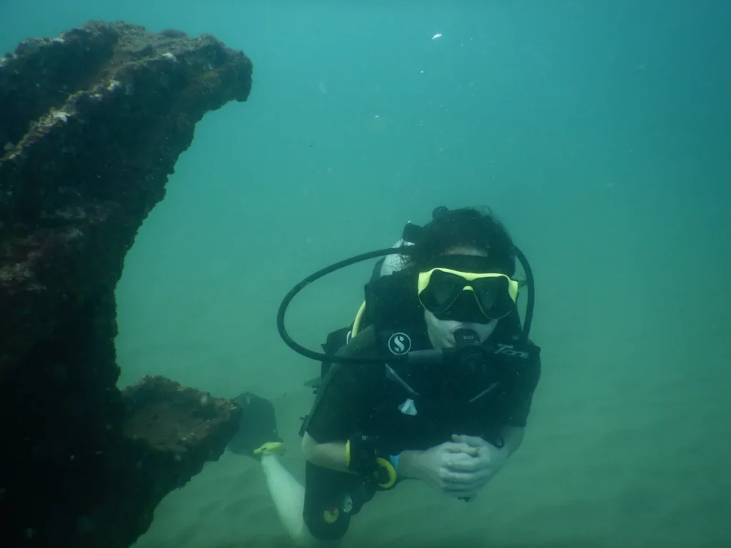 Diver in mask and BCD swimming beside the encrusted structure of Suzy's Wreck, Goa