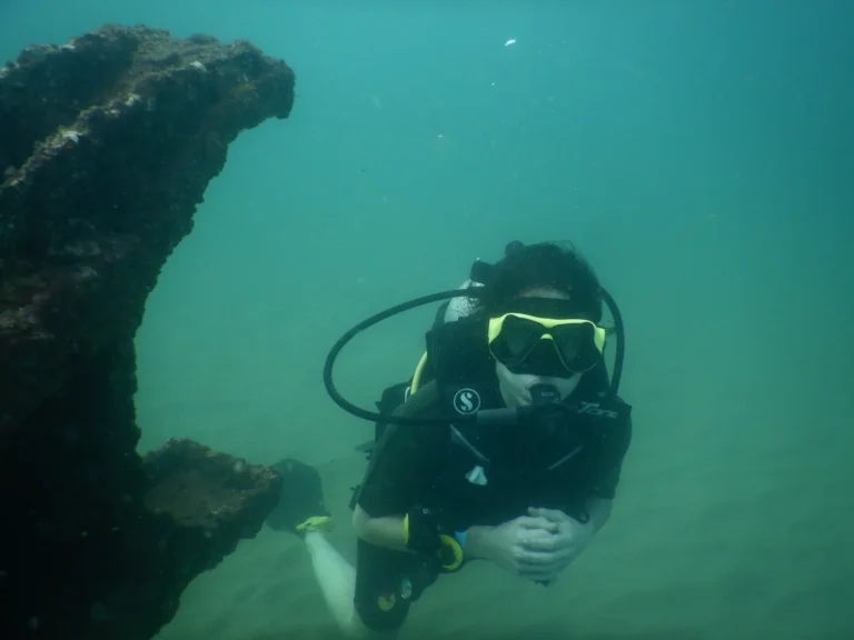 Diver in mask and BCD swimming beside the encrusted structure of Suzy's Wreck, Goa