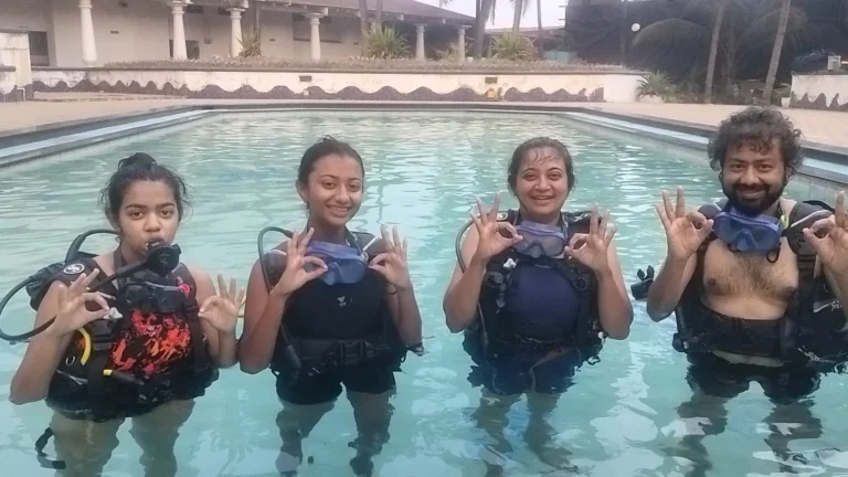 Four students in BCDs line up in the resort pool and make OK signs with both hands