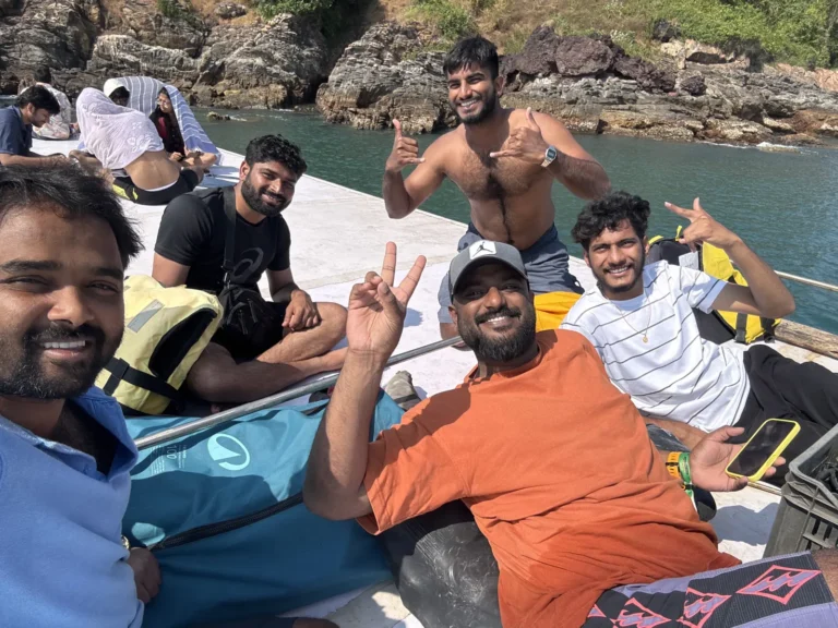 Group of friends grin and give thumbs up for a selfie on the boat deck beside a rocky shore
