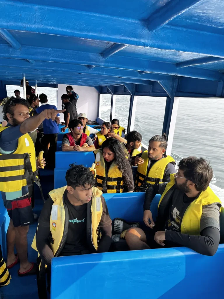 Divers in yellow life jackets sit on the benches of a blue boat cabin on the way to the site