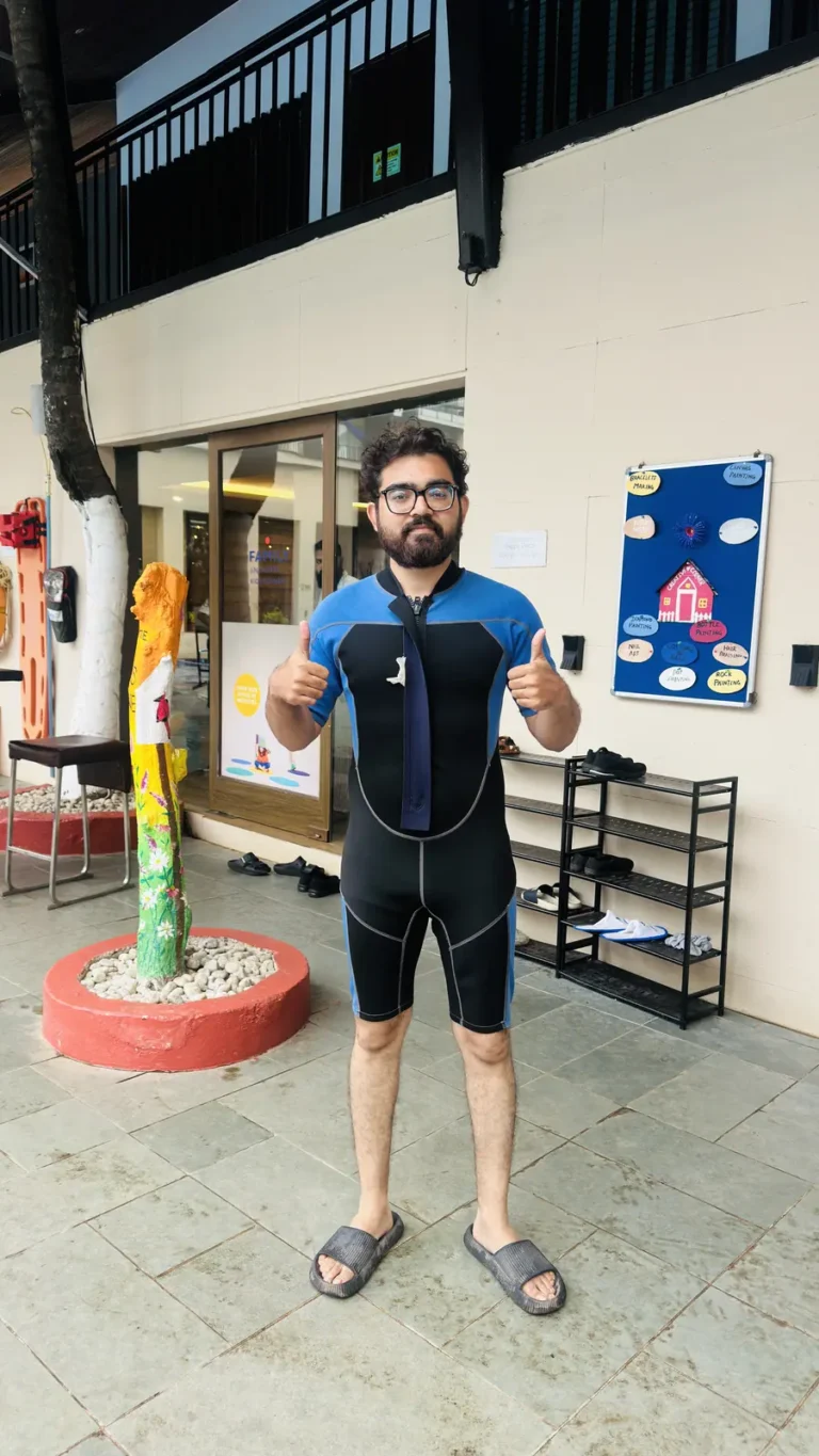 A guest in a shorty wetsuit gives two thumbs up outside the dive centre entrance