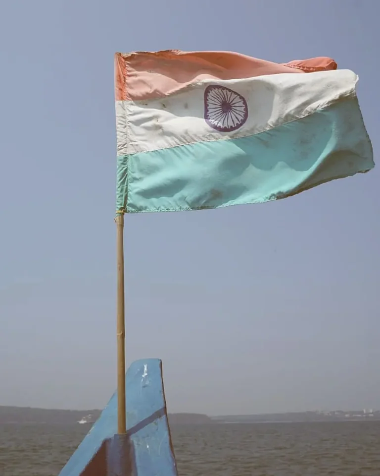 Indian tricolour flag flying from a pole on the blue bow of a boat over hazy open sea