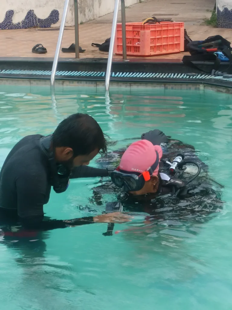Instructor adjusts the gear of a student in a pink swim cap at the shallow end of the pool